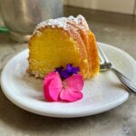 Lemon Cake slice on plate garnished with flowers.