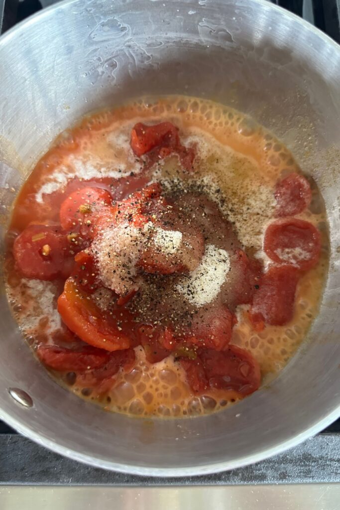 macaroni-ingredients-pot Tomatoes, salt, pepper, and sugar in a pot.