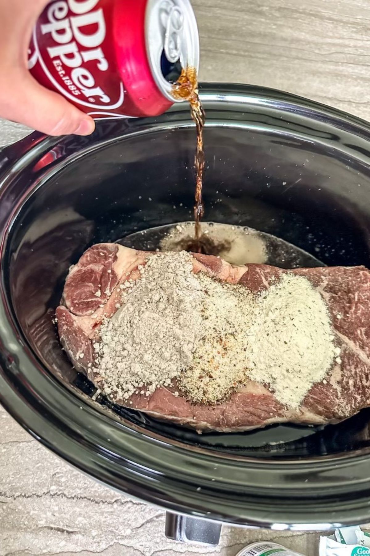 Pouring Dr. Pepper onto the sides of seasoned Pot Roast.