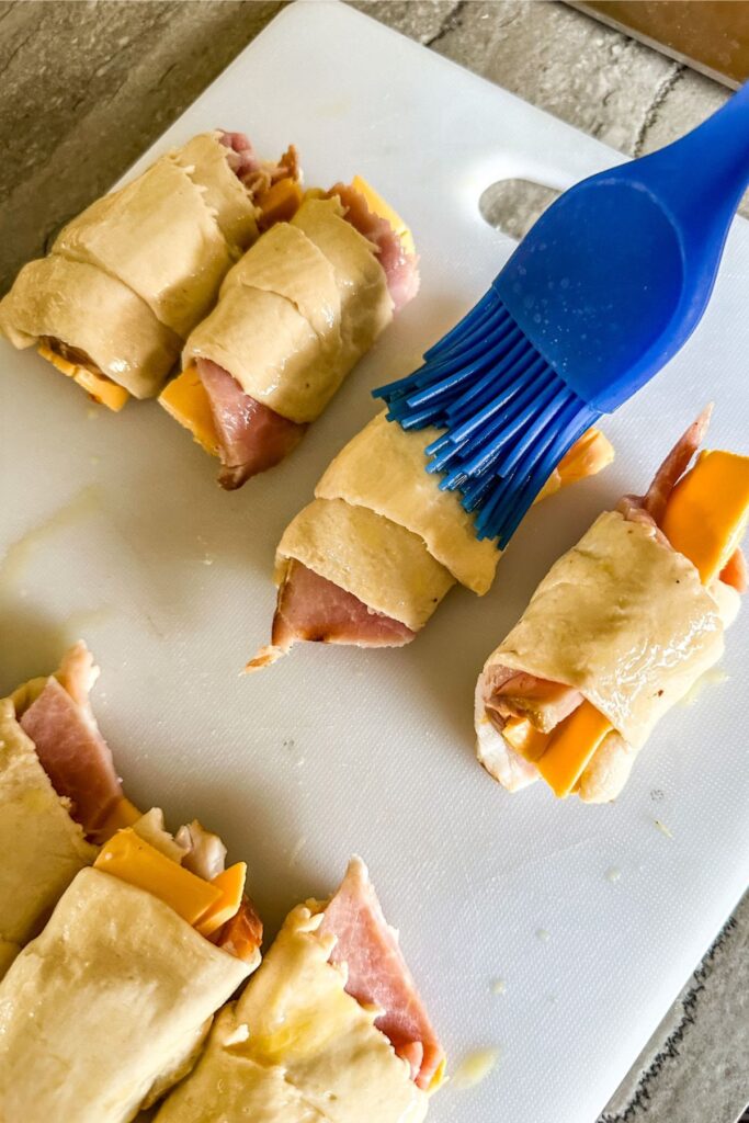 Using a pastry brush to coat the Ham and Cheese Crescent rolls with egg.