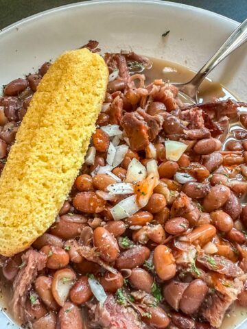 Bowl of Instant Pot Ham and Beans with cornbread and a spoon.