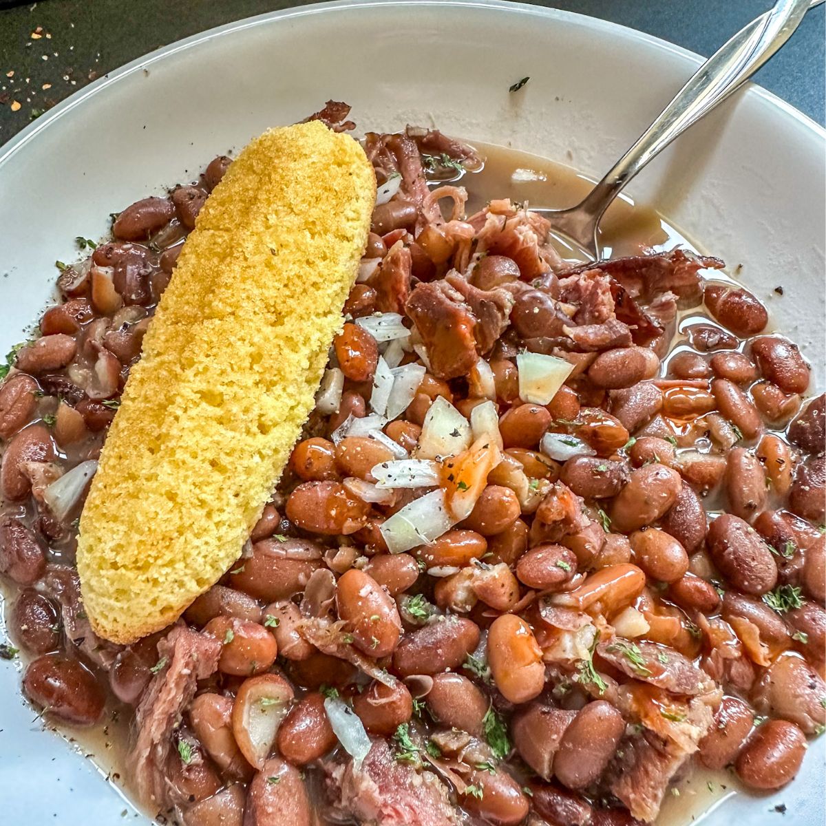 Bowl of Instant Pot Ham and Beans with cornbread and a spoon.