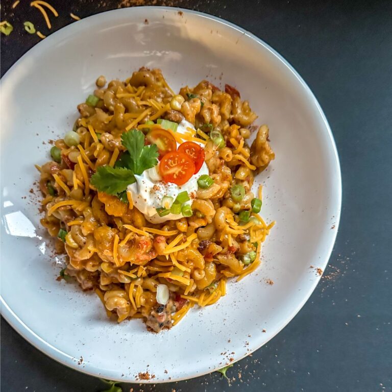 Plate of Mexi Mac and Cheese topped with sour cream, parsley, and tomatoes.