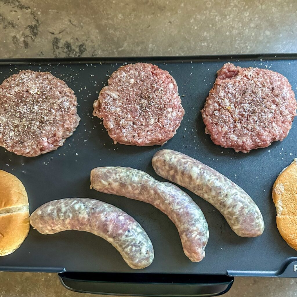 Pork patties and brats on a griddle.