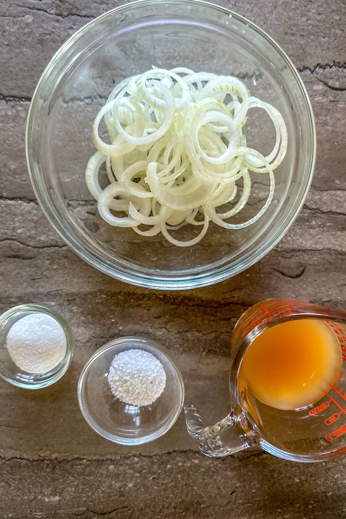 Sliced white onion in a bowl with apple cider vinegar, sugar, and salt. 