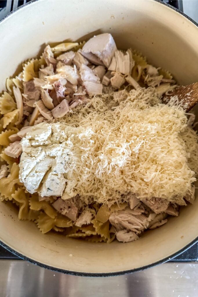 Adding chicken, Boursin cheese, and grated parmesan into cooked pasta.