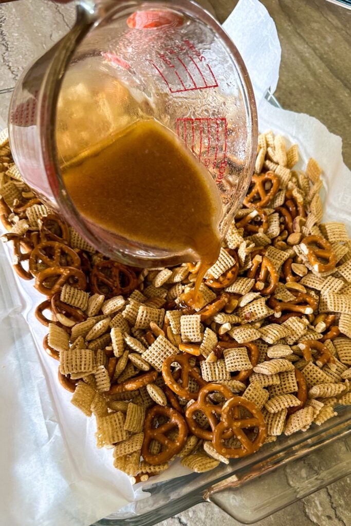 Pouring melted butter, honey, and vanilla mixture onto snack mix.