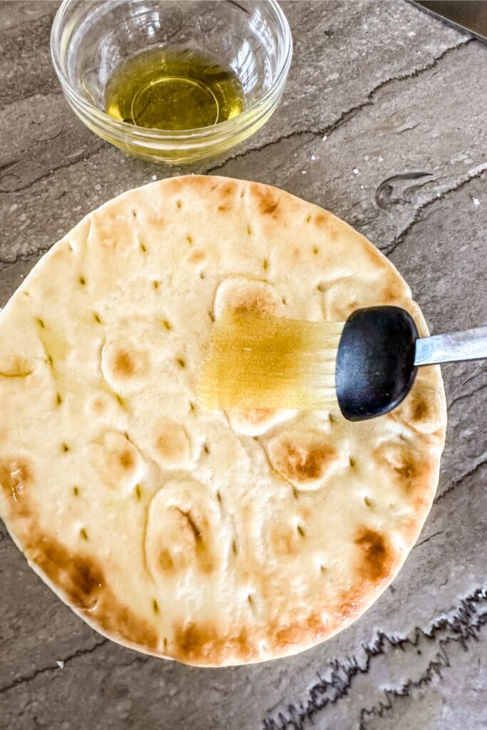 putting olive oil on pita bread.