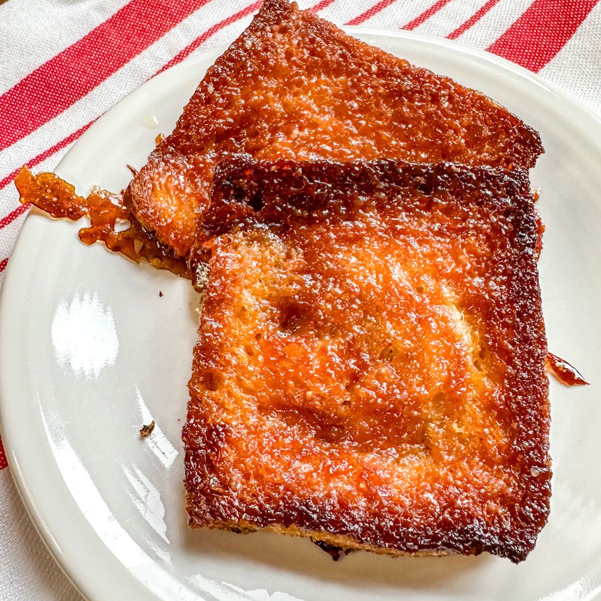 caramelized honey butter toast on a white plate on a red and white table cloth.