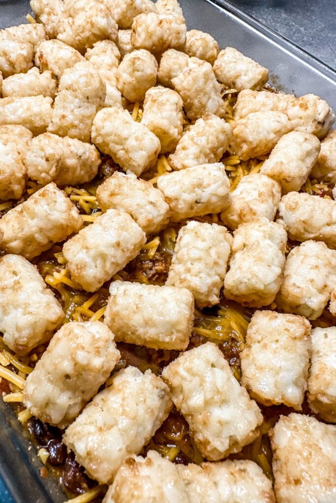 adding tater tots to the chili and cheese to the loaded tater tot casserole.