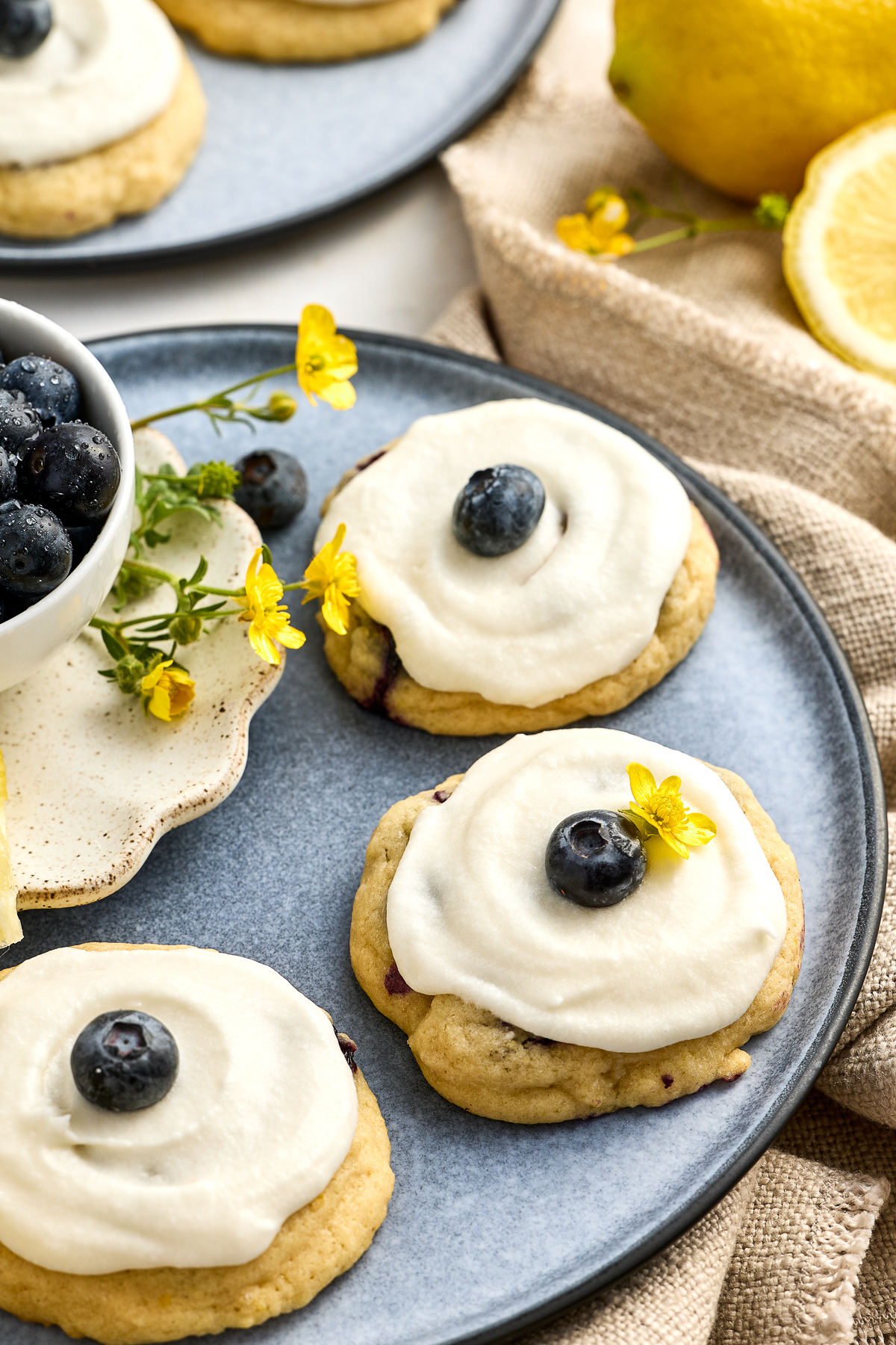 lemon-blueberry-sugar-cookies-topped-with-a-blueberry Lemon Blueberry Cookies served with a blueberry and a yellow flower on top.