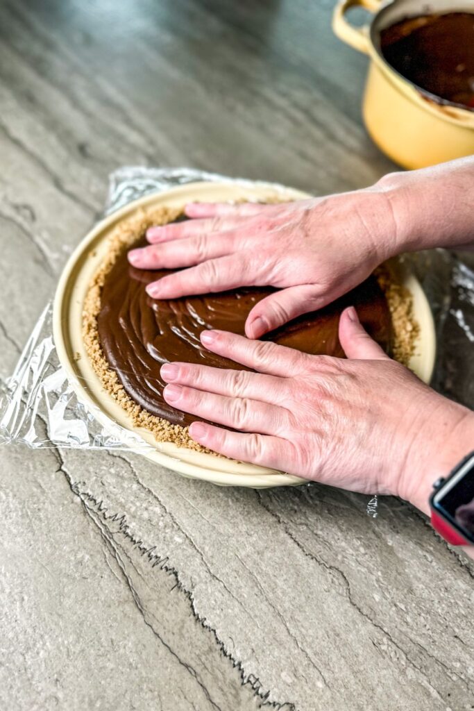 adding-cling-wrap-on-top-of-the-chocolate-cream-pie adding cling wrap to the chocolate cream pie so that it doesn't develop skin on the top of the pie.