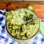 Scooping pesto out of a mason jar with a spoon.