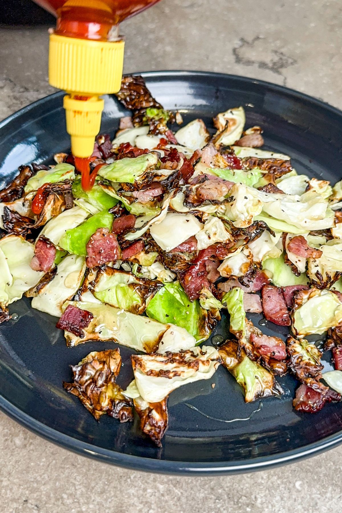 topping the cabbage on the gray plate with sriracha.
