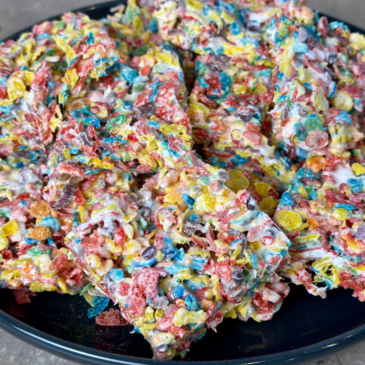 Serving-ready-to-eat-fruity-pebbles-cereal-bars Fruity pebbles cereal bars stacked on a black plate.