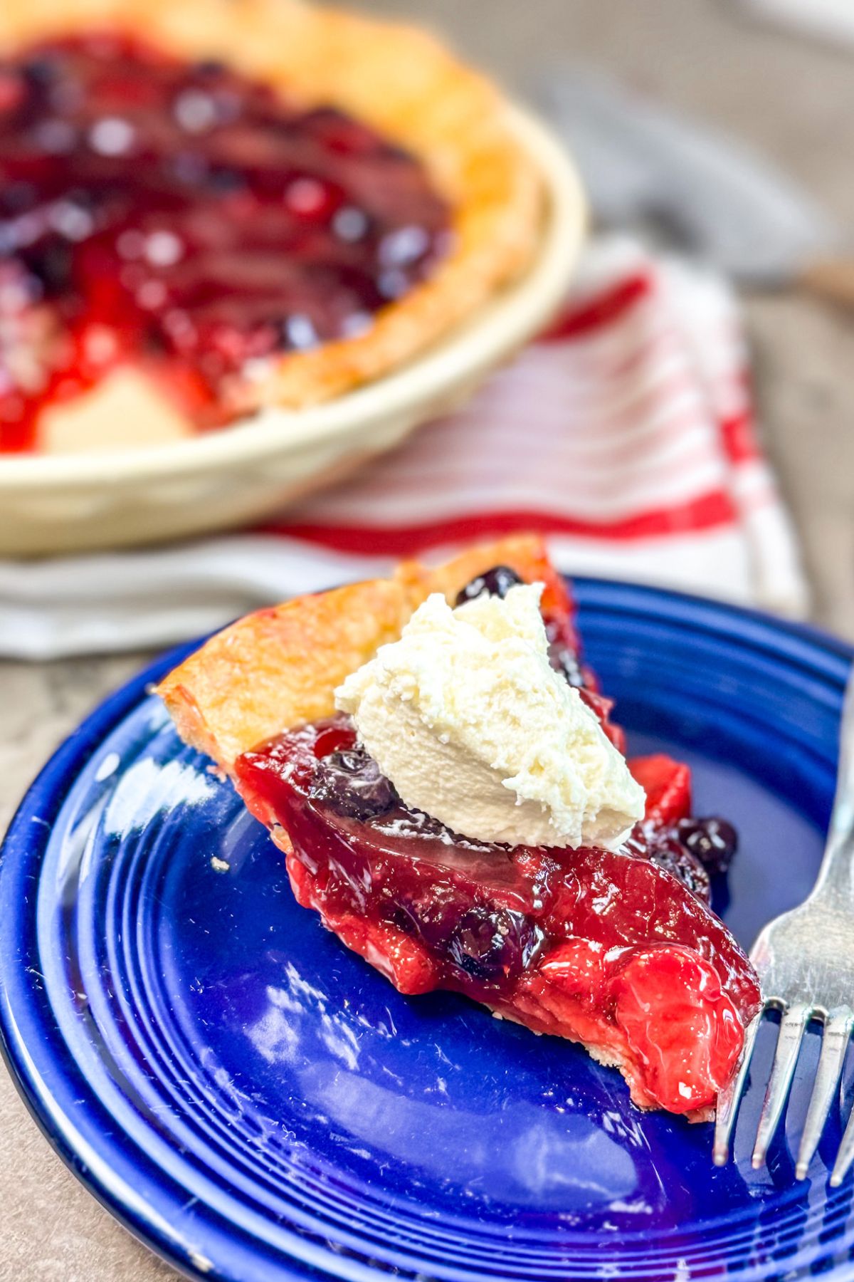 A slice cut out of Blueberry Strawberry Pie and served with whipped topping.