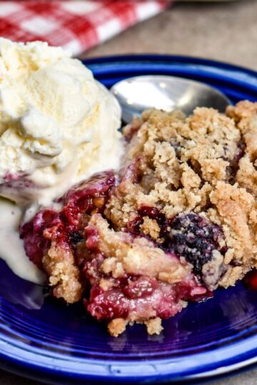 Serving apple and blackberry crumble to my party guests in a navy blue bowl.