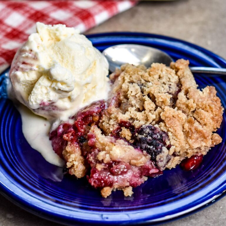 Serving apple and blackberry crumble to my party guests in a navy blue bowl.