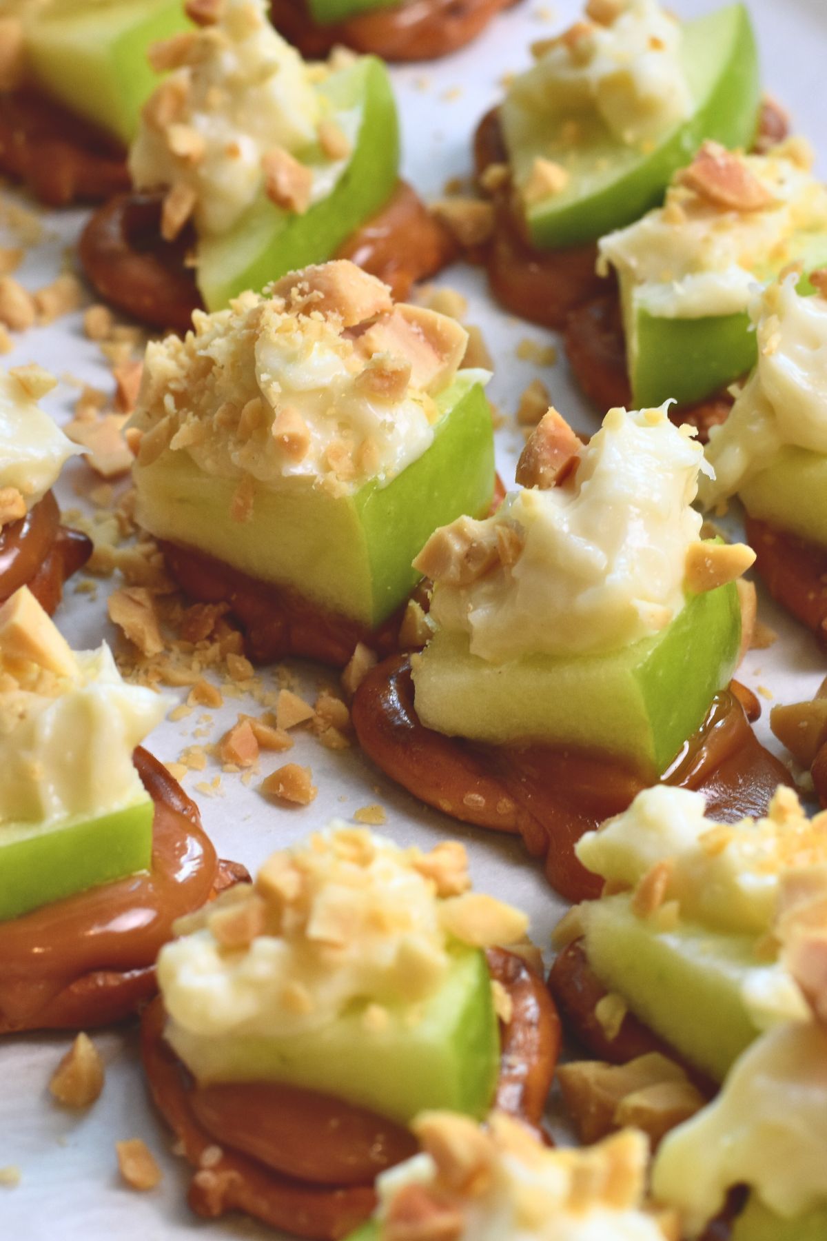 Caramel apple bites are topped with cream cheese dip and chopped pretzels.