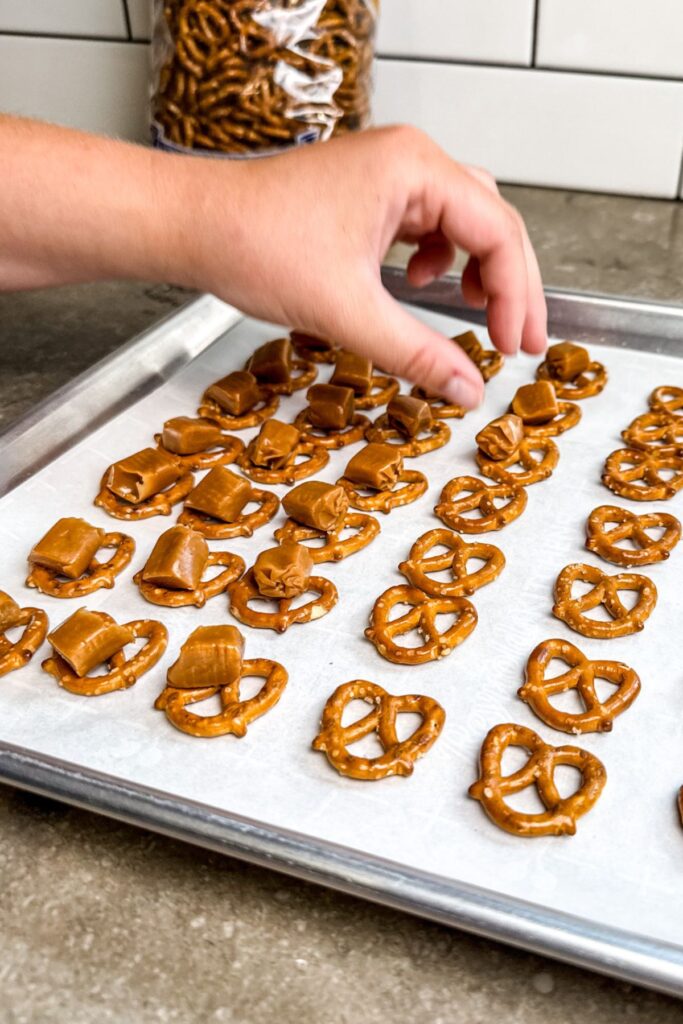 Adding the caramel candies on to the pretzel. Then, place them in the oven to melt.