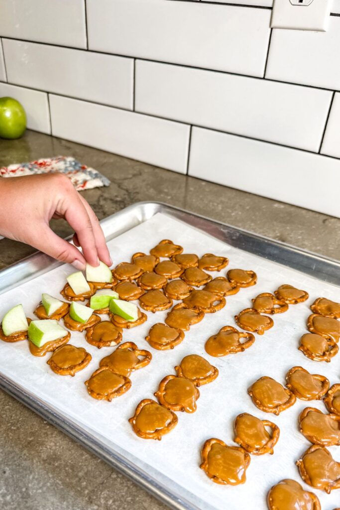 Topping the melted caramel with apple slices while still hot.