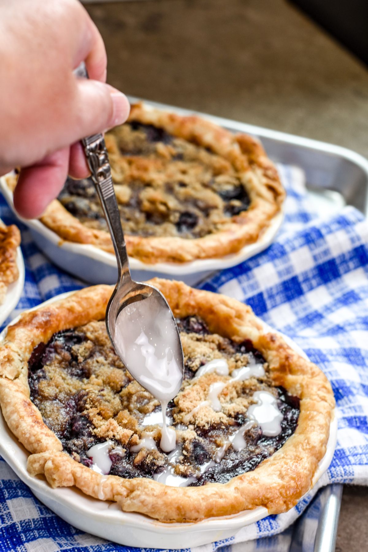adding-the-icing-on-to-the-blueberry-pies drizzling powdered sugar icing on top of mini blueberry pies.