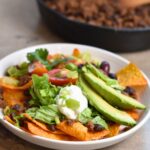 taco salad topped with avocado, lettuce, sour cream, and green onions.