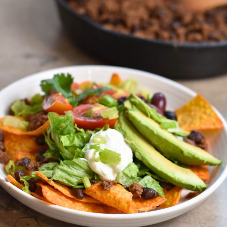 taco salad topped with avocado, lettuce, sour cream, and green onions.