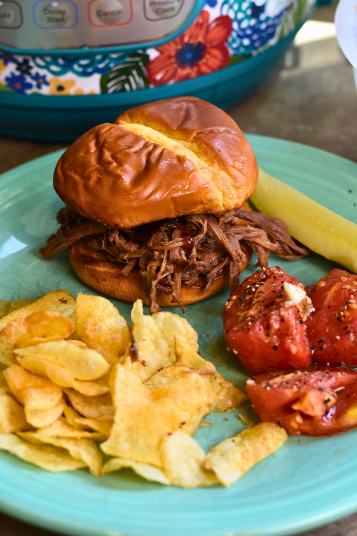 shredded-beef-served-for-family-dinner-as-a-BBQ-sandwich Serving the shredded beef as a sandwich with chips and a pickle.