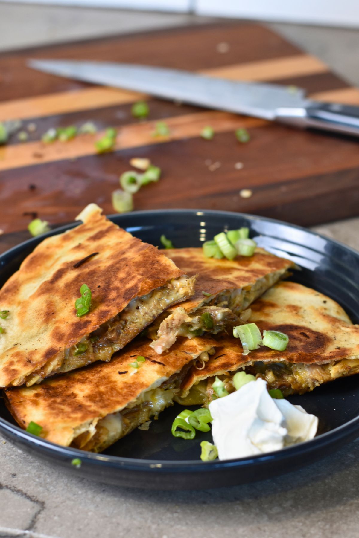 Serving-the-quesadilla-with-sour-cream-and-green-onions Ready to eat pulled pork quesadilla.