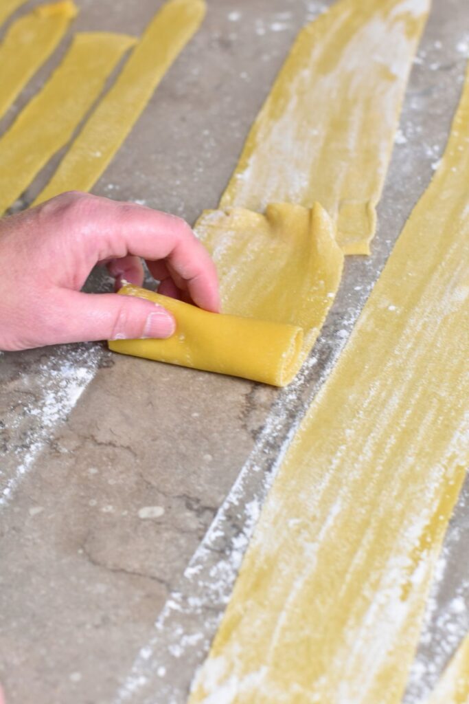 turn-strips-into-rolls rolling up the homemade pappardelle pasta and then cutting them.