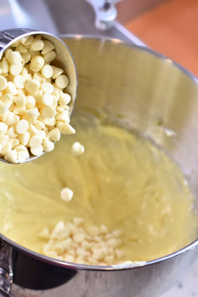 Bowl-of-cream-cheese-filling-with-white-chocolate-chips Pouring white chocolate chips into a bowl of cream cheese filling.
