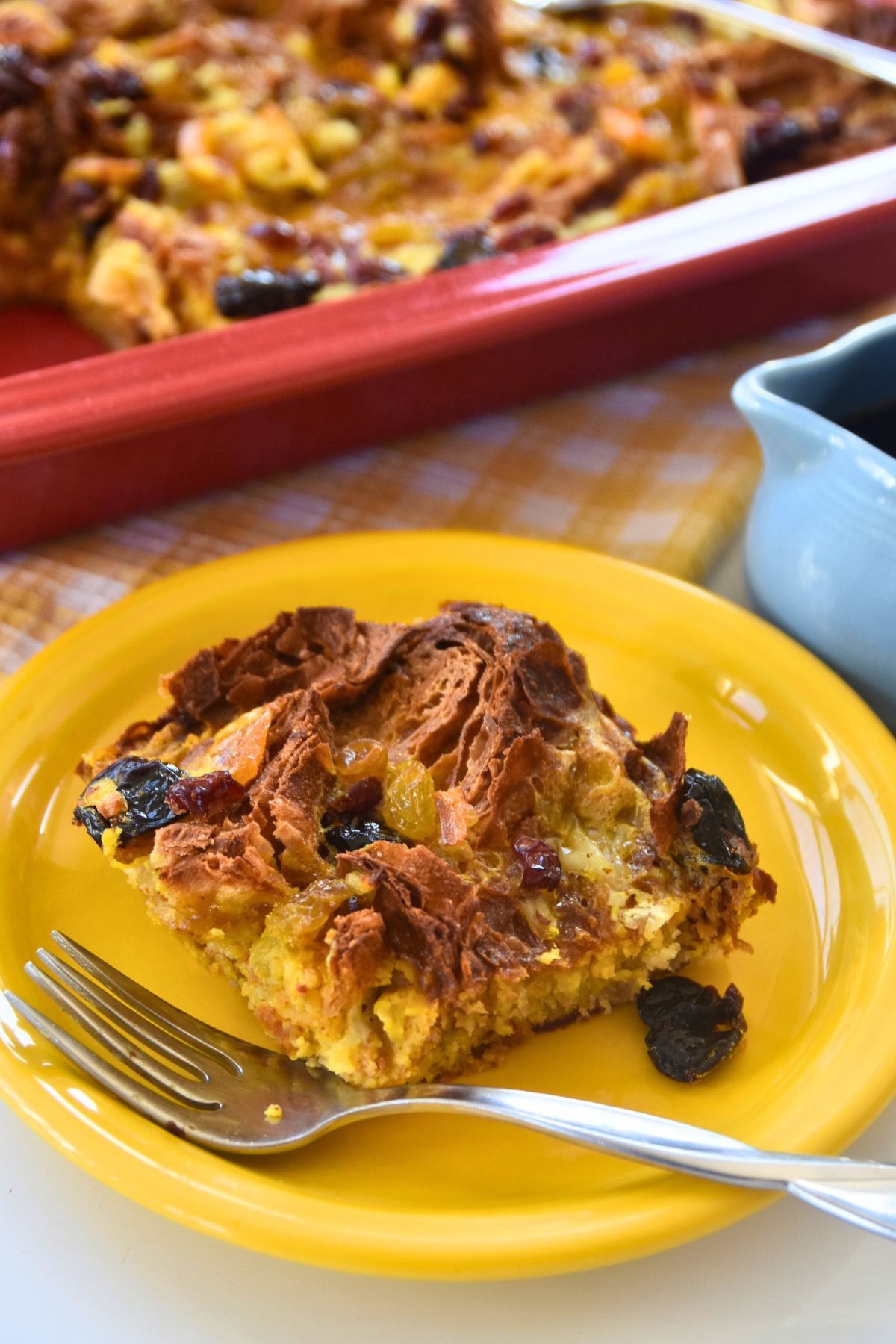 sweet-golden-brown-croissant-breakfast-casserole-being-served-to-guest Serving croissant breakfast casserole on a yellow plate.