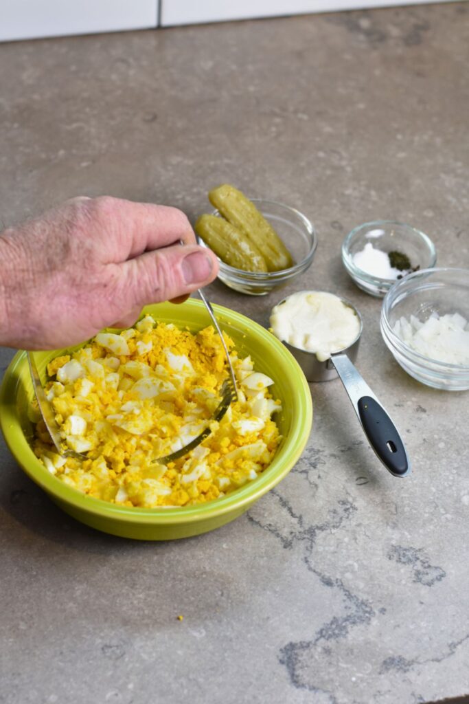 mashing-boiled-eggs-for-dill-pickle-egg-salad Mash the eggs and add the mayo, pickles, seasoning, and onion.