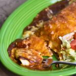 Eating the burrito enchilada with lettuce and a tomato.