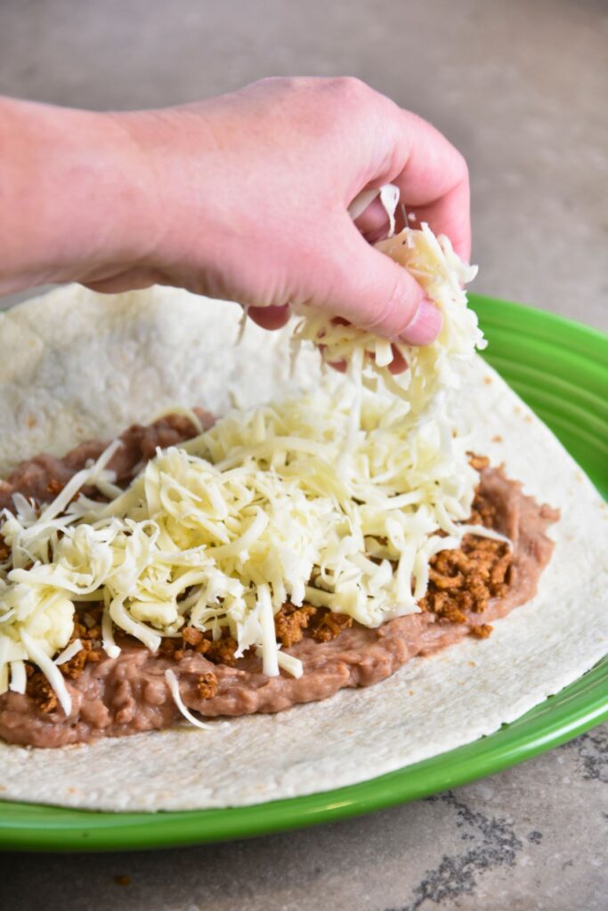 broil-the-cheese-to-top-of-the-burrito-and-serve-with-shredded-lettuce Sprinkling cheese in the burrito enchilada.