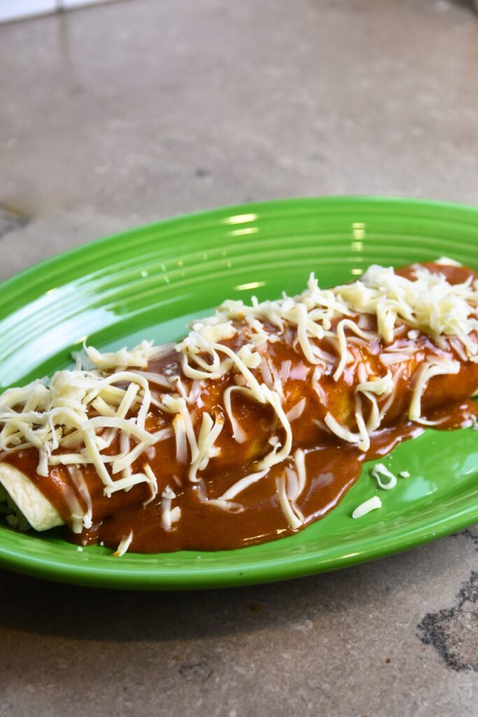 pour-the-enchilada-sauce-on-top-the-burrito-and-sprinkle-with-cheese Burrito enchilada topped with cheese and ready to go into the oven.