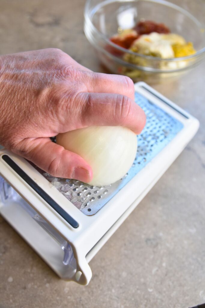 use-a-cheese-grater-to-shred-the-yellow-onion grating the yellow onion with a cheese grater.