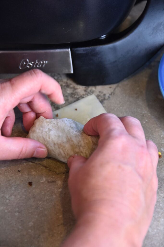 Fold-the-spring-roll-wrapper-into-a-burrito Rolling up the cheeseburger spring rolls.