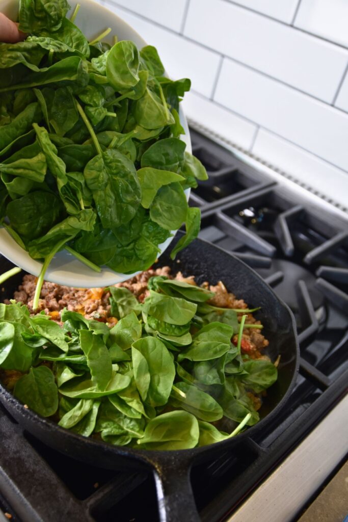 add-the-spinach-into-the-sausage Adding the spinach into the skillet.