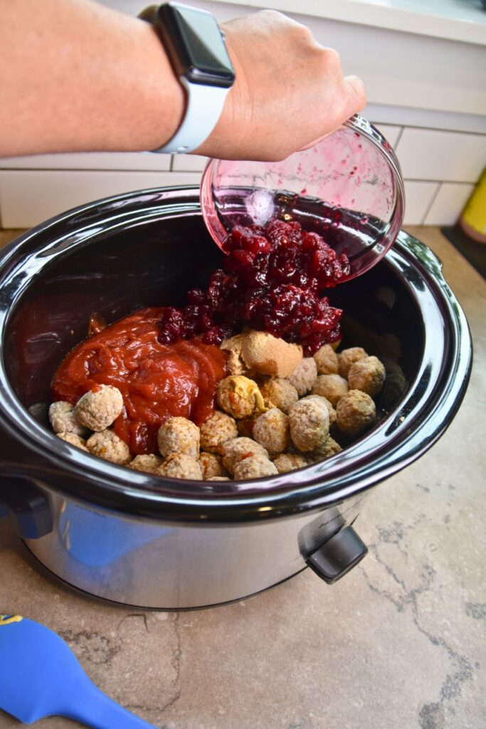 add-the-cranberries-and-chili-sauce-to-the-meatball-mixture Pour the cranberries on top of the meatball mixture.