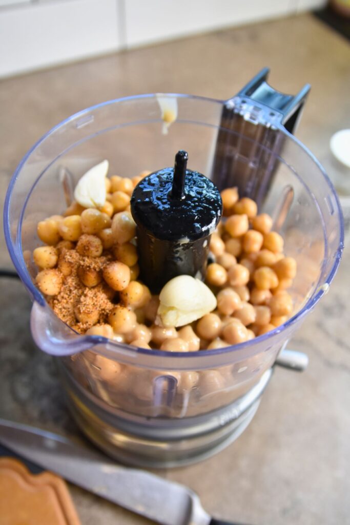 Blend-the-garlic-chickpeas-and-seasoning-in-the-food-processor Using a food processor to blend chickpeas until smooth.