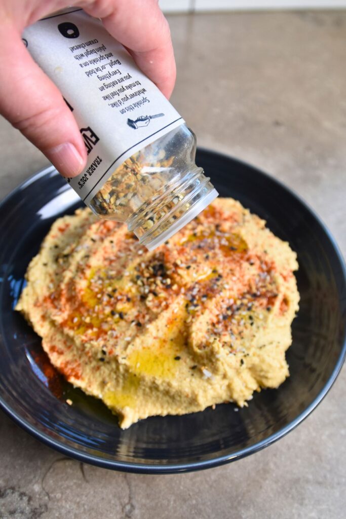 Sprinkle-everything-bagel-seasoning-on-top-of-the-hummus Topping the hummus with everything bagel seasoning.