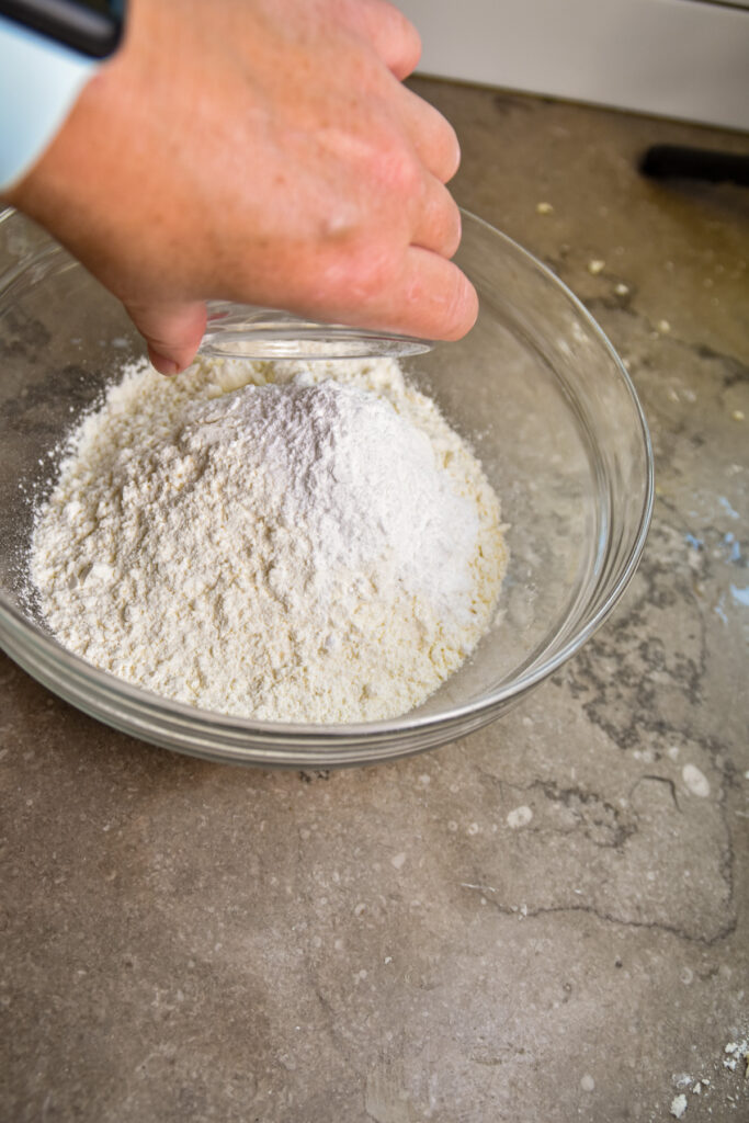 adding-baking-powder-to-biscuits Pouring baking soda and salt into flour for skillet biscuits