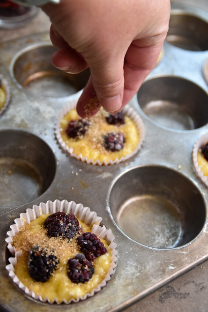 sprinkling raw sugar on blackberry muffin
