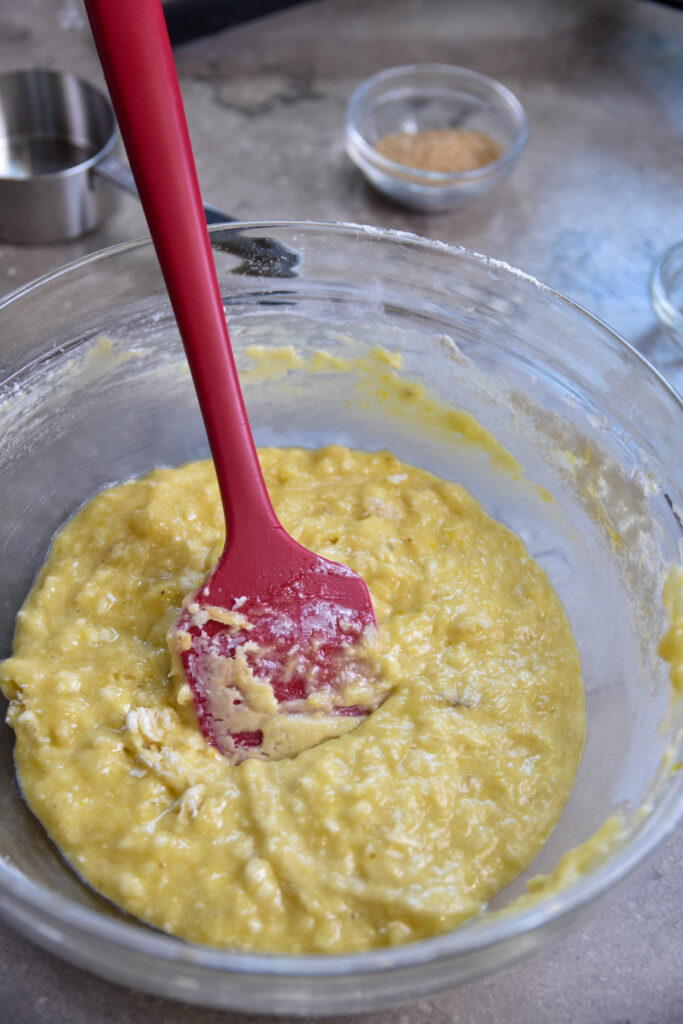 muffin batter in clear bowl with red rubber scraper