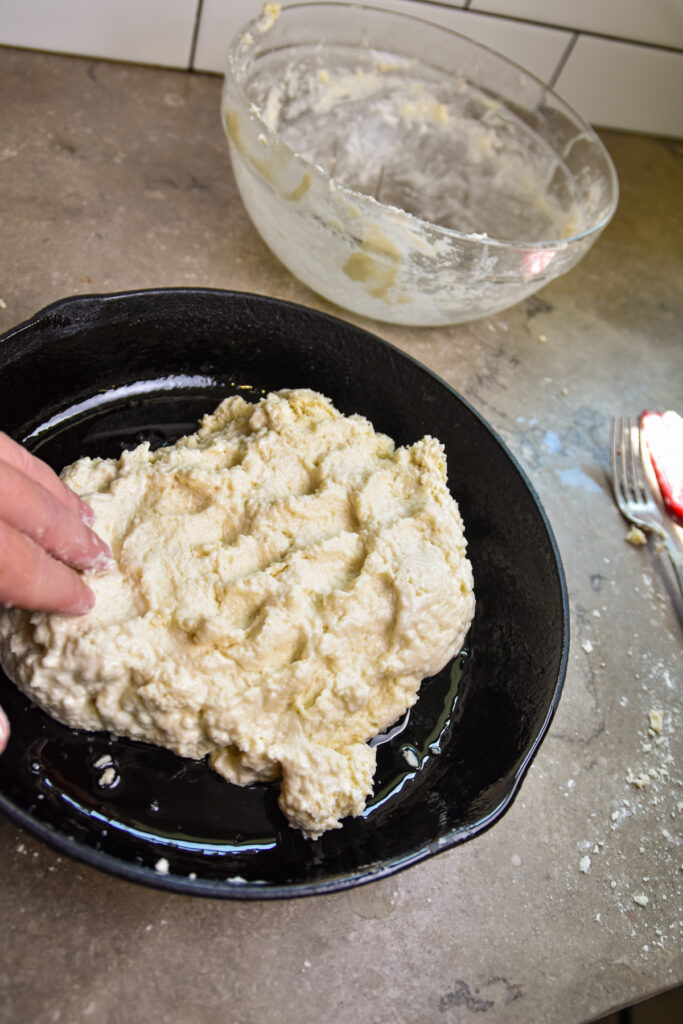 press-biscuit-dough-in-pan Pressing skillet biscuit dough into an iron skillet