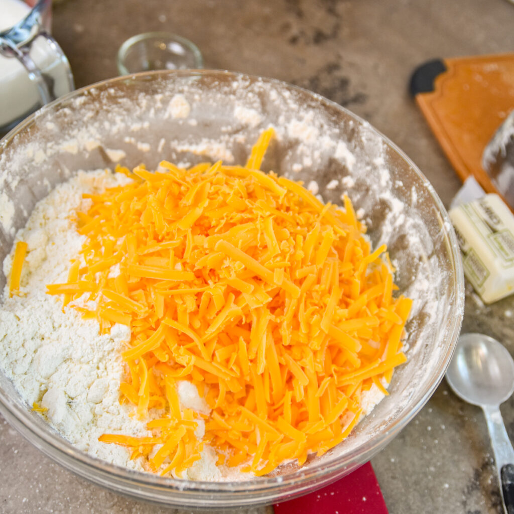 Adding cheese to biscuit mix in a class bowl.