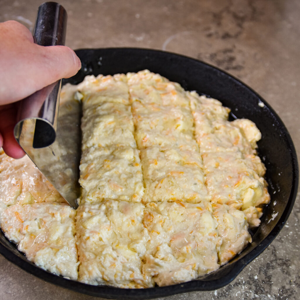 Cutting cheddar bay biscuits before baking in iron skillet.