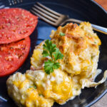 Plated serving of chicken bacon ranch casserole with two biscuits and a side of tomato slices.